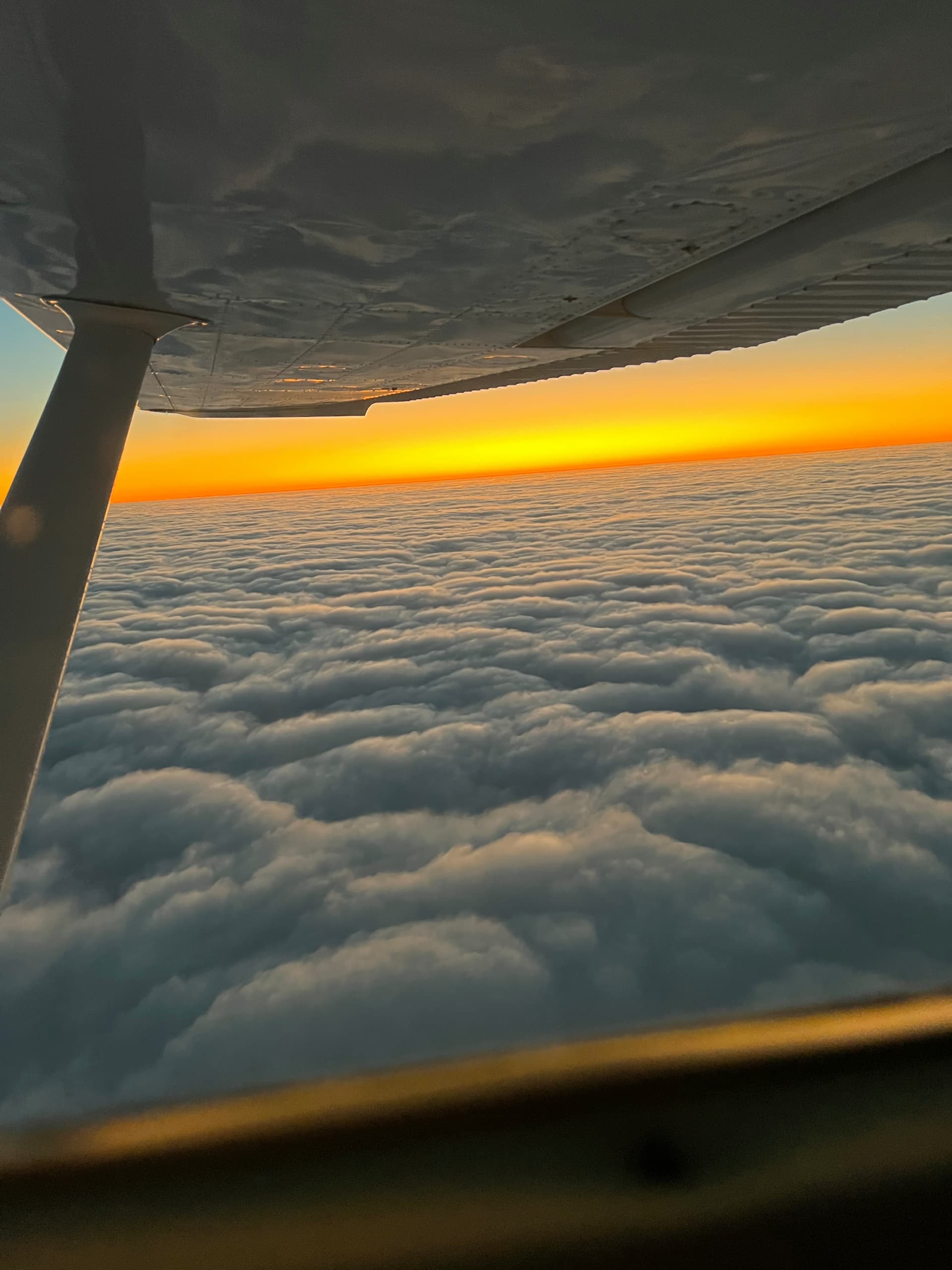 The view under a Cessna's wing above a cloud layer at a fiery sunset