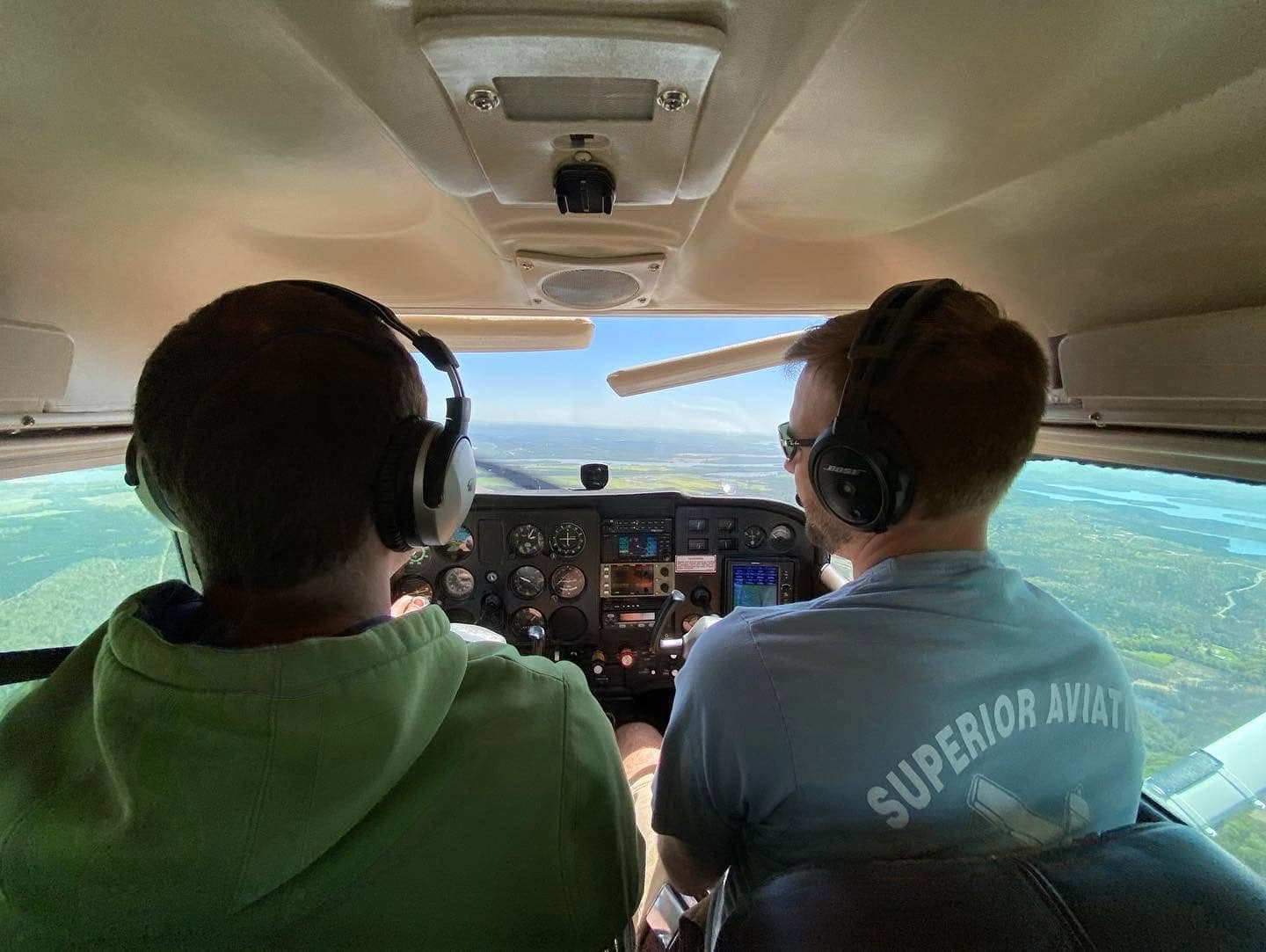 A student and a Superior Aviation instructor in the cockpit mid-flight, looking out over the green Arkansas landscape