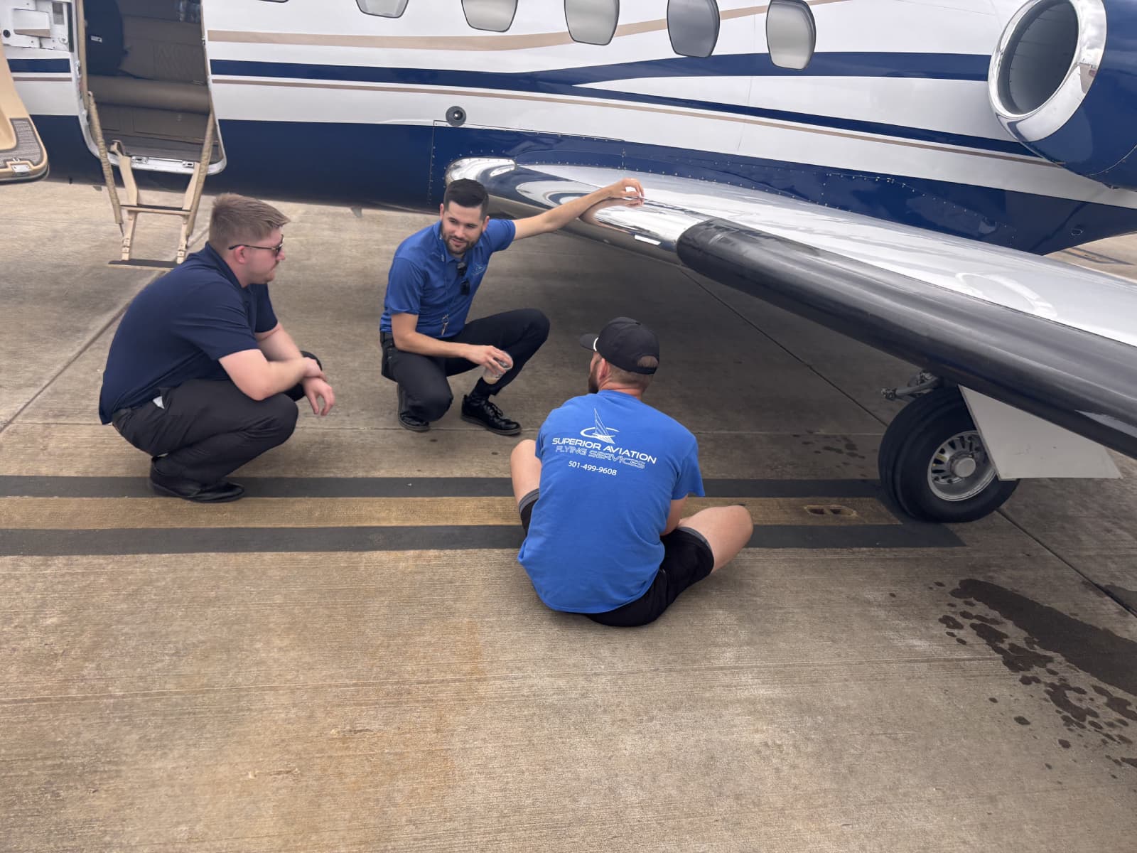 Three Superior Aviation members gathered around the wing of a twin-engine business jet on the ramp